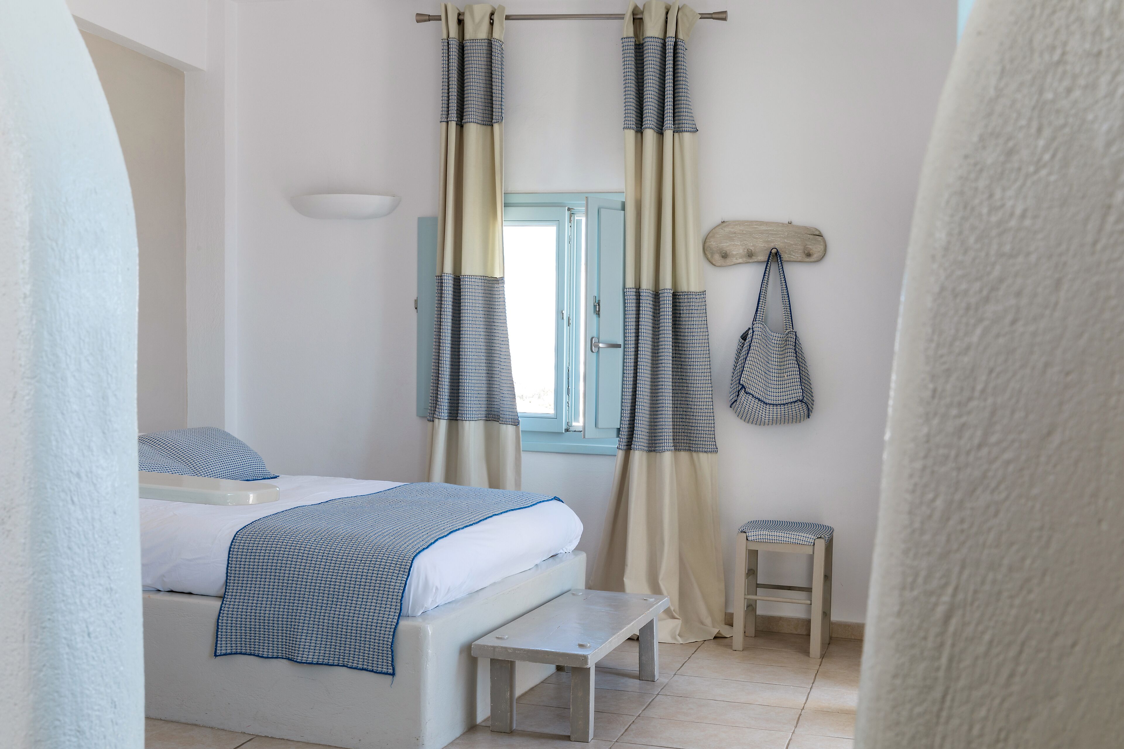 Ein Schlafzimmer mit Bett, Bank, Vorhängen und einem kleinen Hocker.