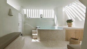 Un baño moderno con bañera, un mueble de madera, una planta en maceta y un banco.