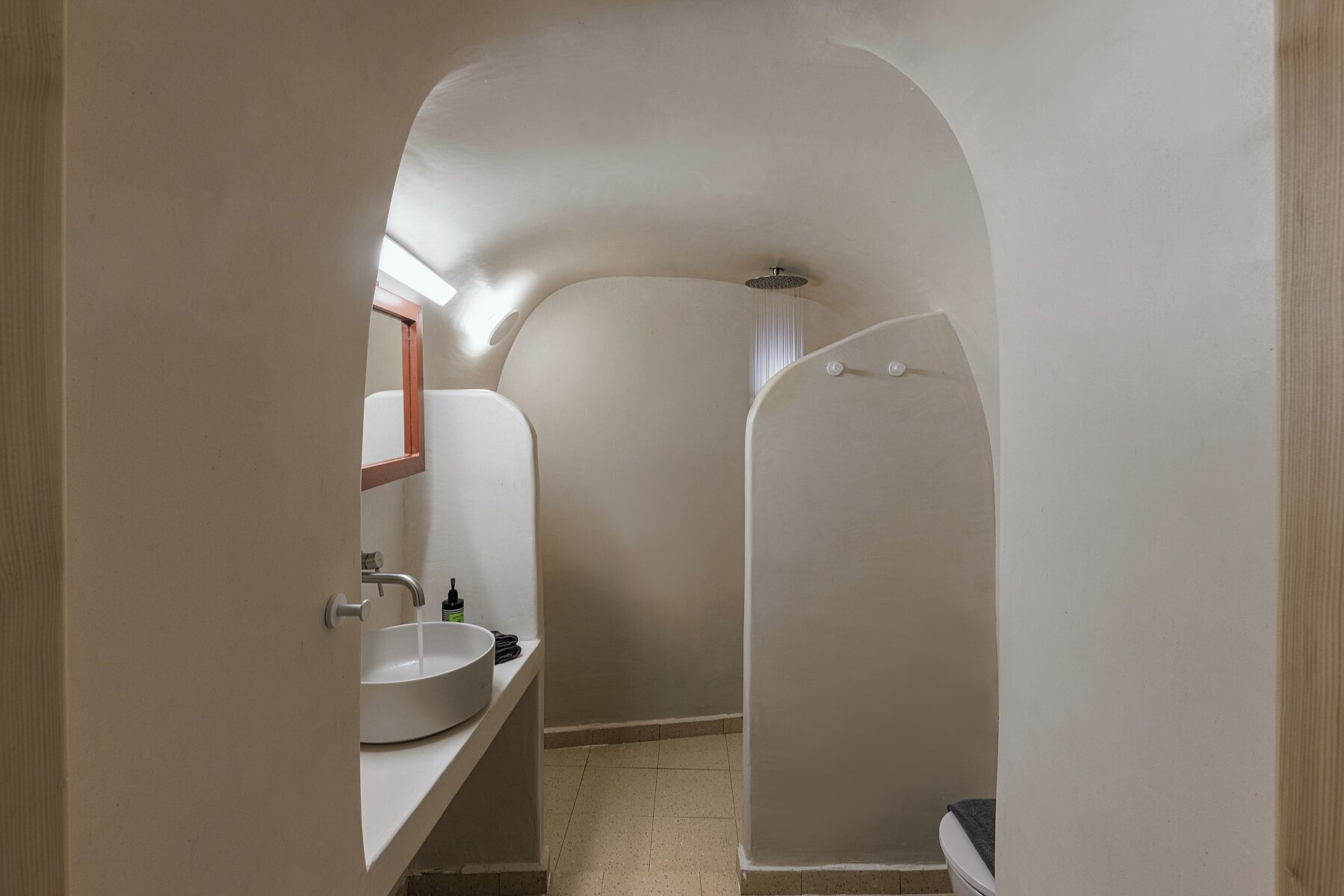 A narrow bathroom with a white sink, a mirror, and a shower area.