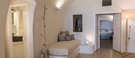 A bedroom with a bed, bedside table, lamp, and a view into another room.