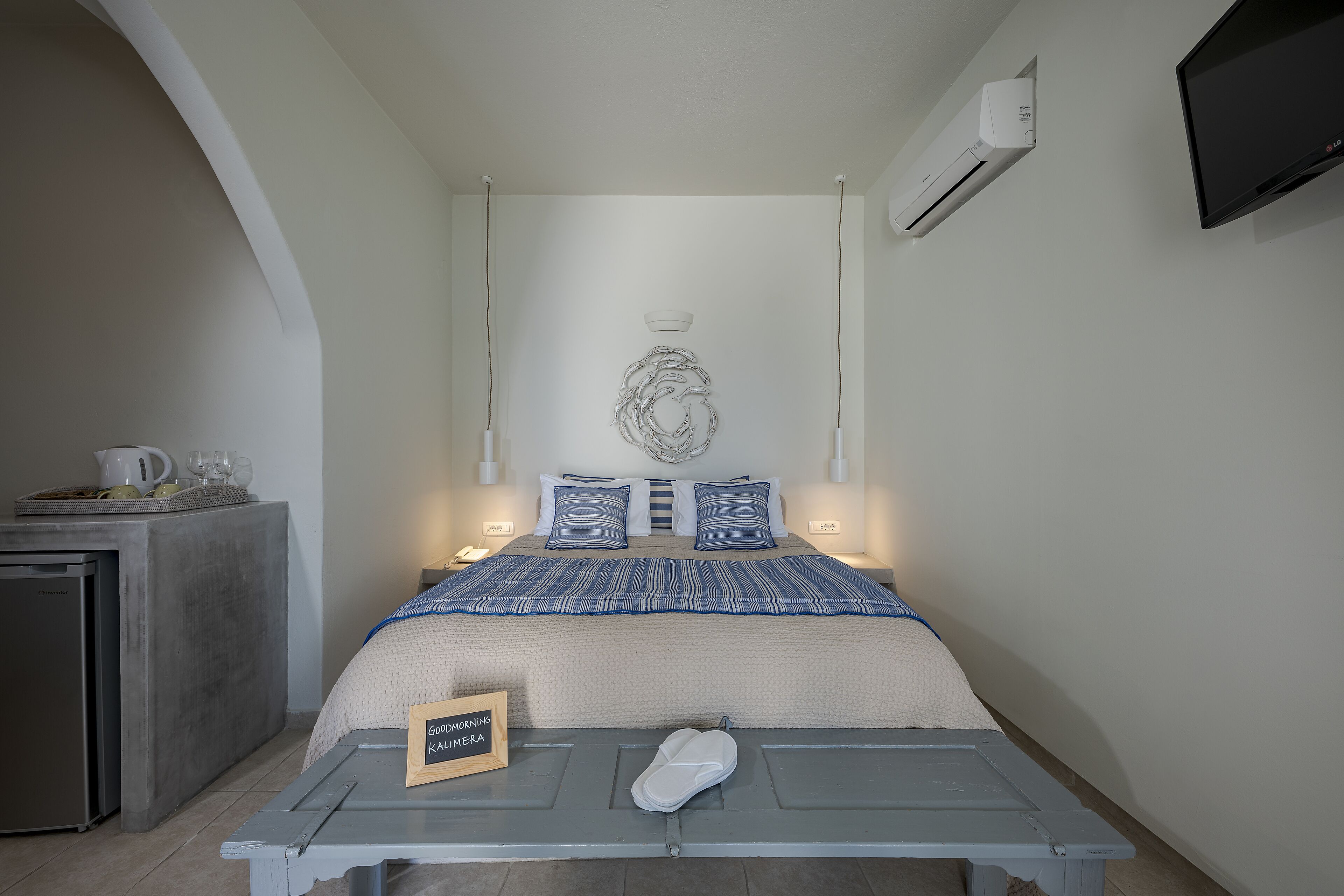 A bedroom with a bed, bedside tables, a desk, a flat-screen TV, and an air conditioning unit.