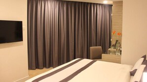 A hotel room with a large bed, a flat-screen TV mounted on the wall, a desk with a vase of flowers, and a chair. - NU Hotel (Kuala Lumpur)