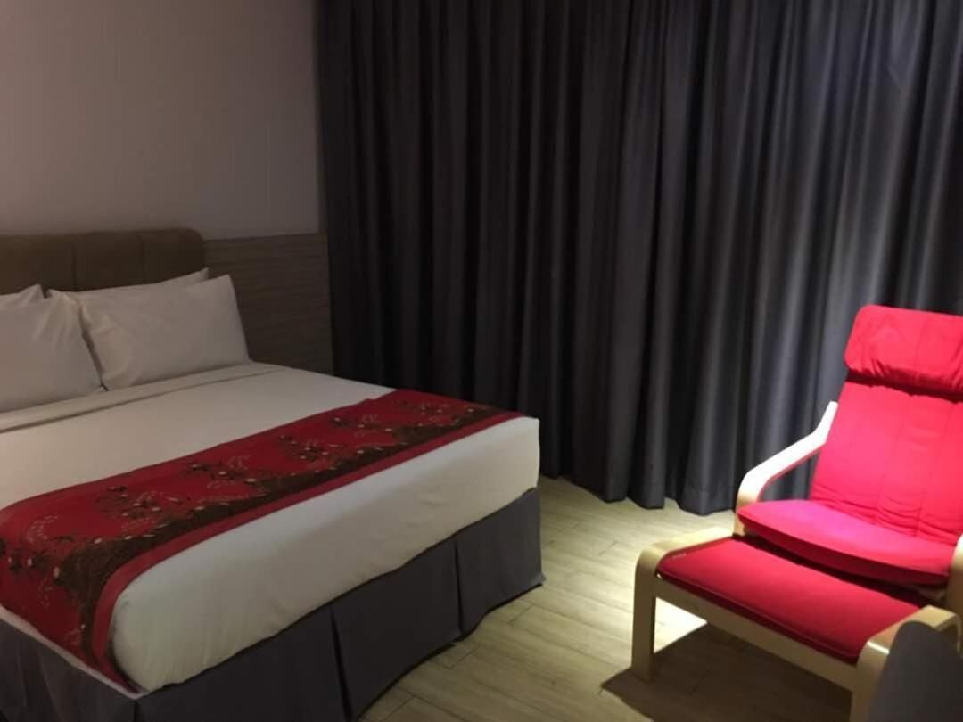 A hotel room with a bed, a red chair, and dark curtains.
