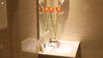 A bathroom with a sink, mirror, and a vase with flowers.