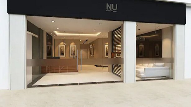 A modern hotel entrance with a minimalist design, featuring a reception area with a sofa and a coffee table, and a visible bathroom with a sink and mirror. - NU Hotel (Kuala Lumpur)