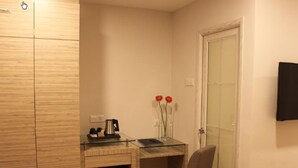 A compact room with a wooden wardrobe, a glass desk with a chair, a coffee maker, and two red flowers. - NU Hotel (Kuala Lumpur)
