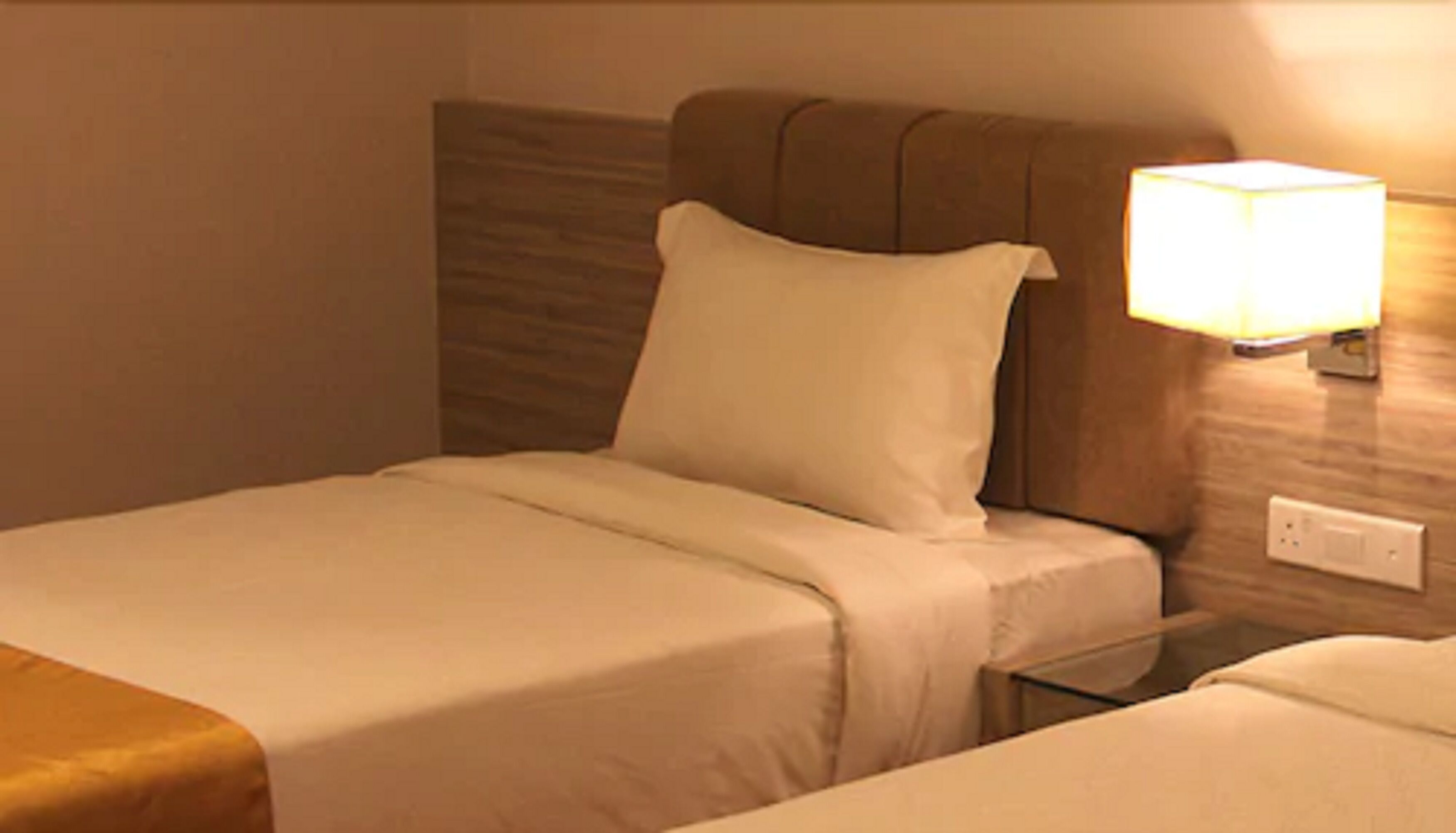 A hotel room with two beds, a nightstand, a wall-mounted lamp, and a power outlet.