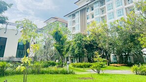 Un edificio moderno con varios pisos, amplias ventanas y un jardín cuidado con diversas plantas y árboles.
