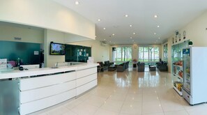 A modern hotel lobby with a reception desk, seating area, and a large window offering a view of trees. - Harmony Resort Hotel (Chiang Mai)