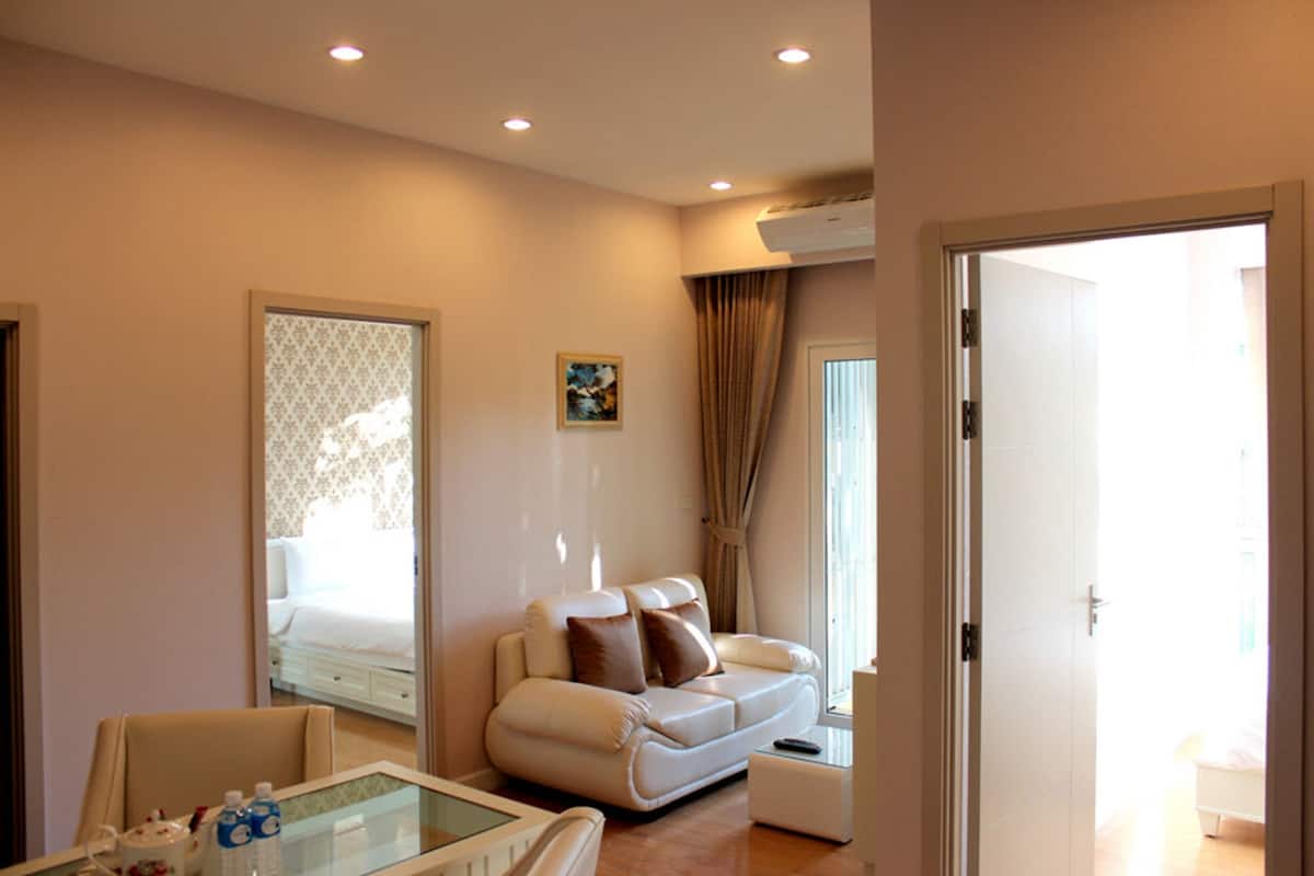 A hotel room with a sofa, a glass table, a bed, and an air conditioning unit.