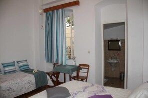 A bedroom with two beds, a dining table, and a bathroom with a sink and mirror. - Medieval Rose Hotel (Rhodes)