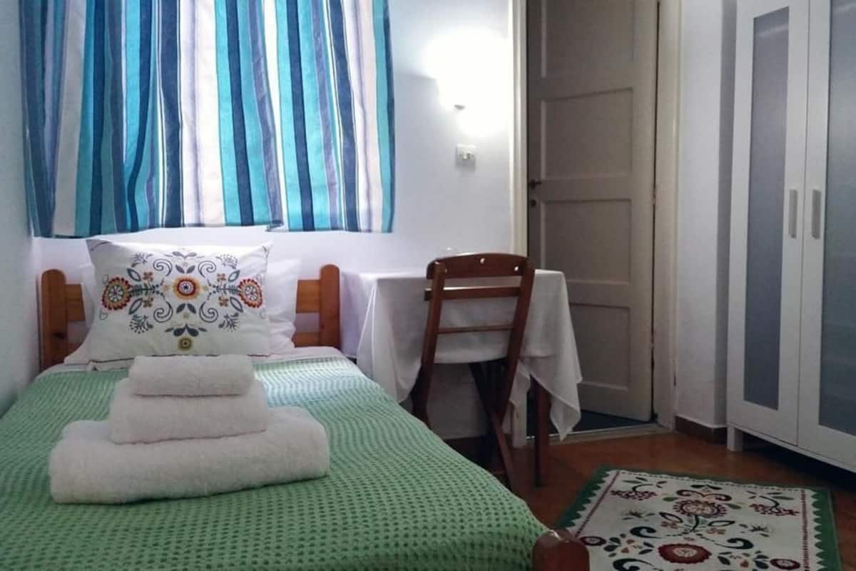 A room with a bed, a chair, a table, and a wardrobe.