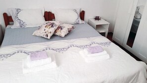 A neatly made bed with a patterned bedspread, two pillows, and two folded towels. - Medieval Rose Hotel (Rhodes)