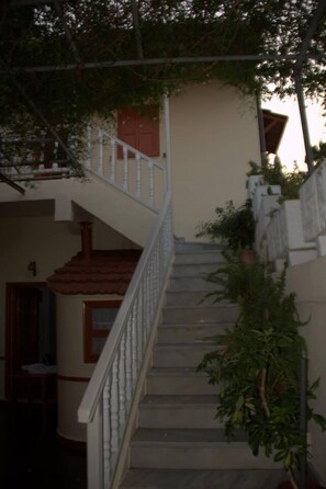 A staircase leading to a second floor with a white railing, surrounded by greenery and a beige wall. - Medieval Rose Hotel (Rhodes)
