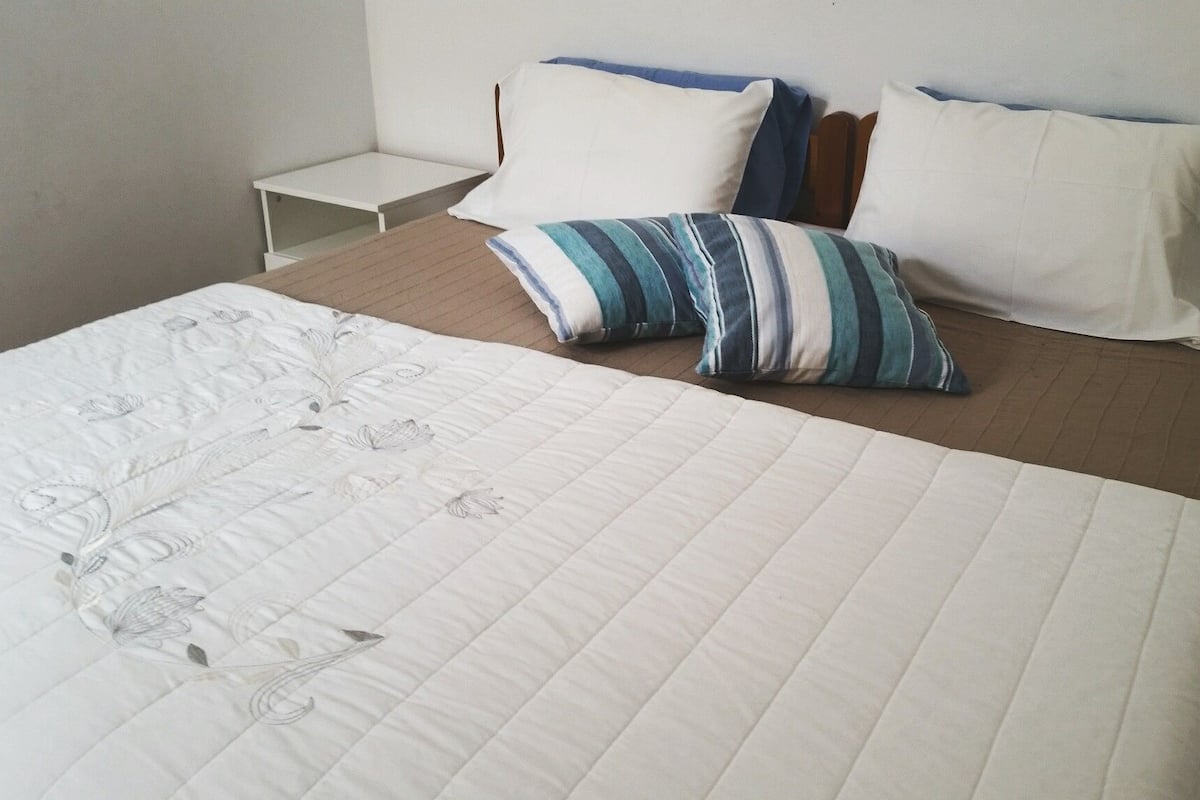 A neatly made bed with a floral-patterned duvet, a striped pillow, and a plain pillow on a wooden headboard.