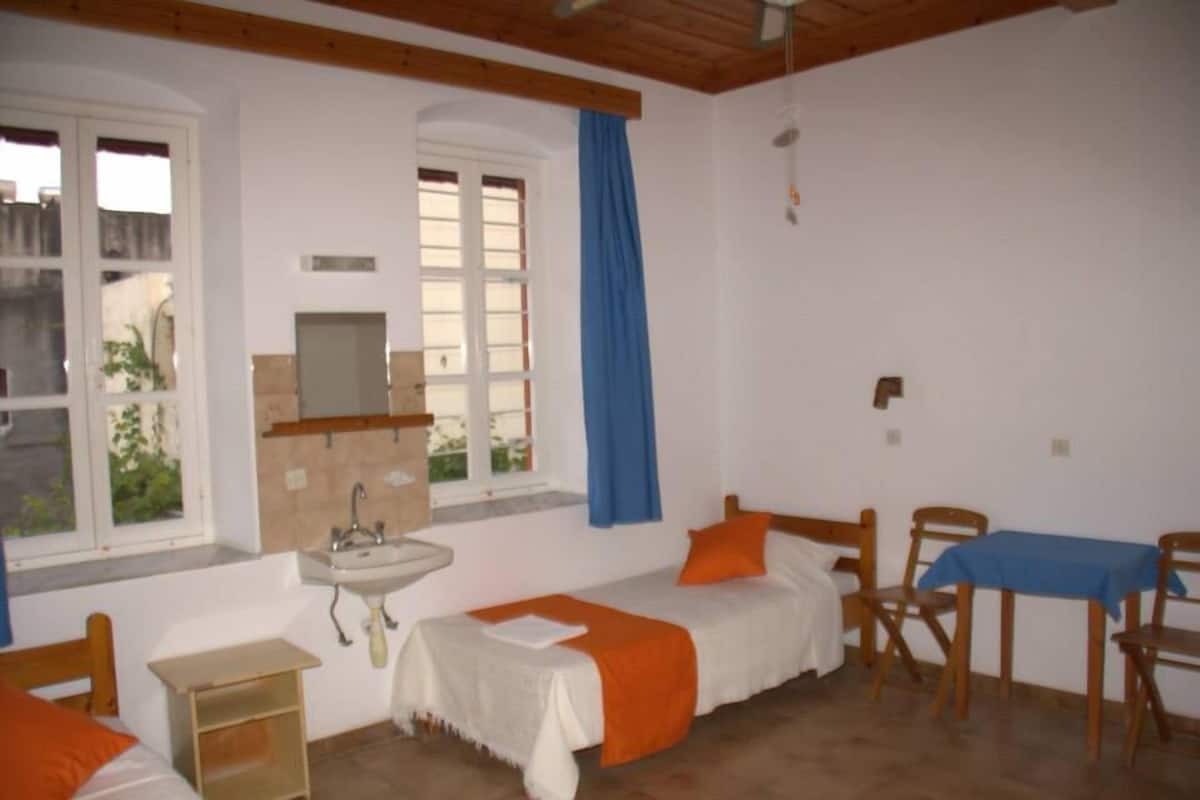 A small, clean room with two beds, a sink, and a table.