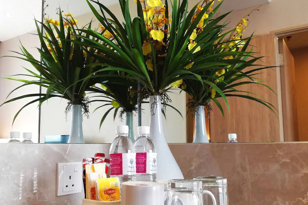 A kitchen counter with a tray holding a coffee maker, two cups, and a bottle of Lipton tea. There are also two vases with yellow flowers and a water dispenser.