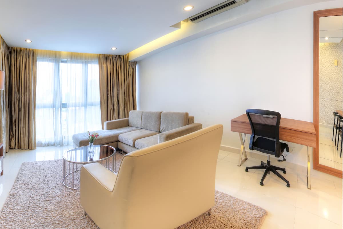 A modern hotel room with a flat-screen TV, a sofa, a coffee table, a desk with a chair, and large windows with curtains.