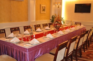 A long dining table set for a formal meal with chairs, a vase of flowers, and a television mounted on the wall.