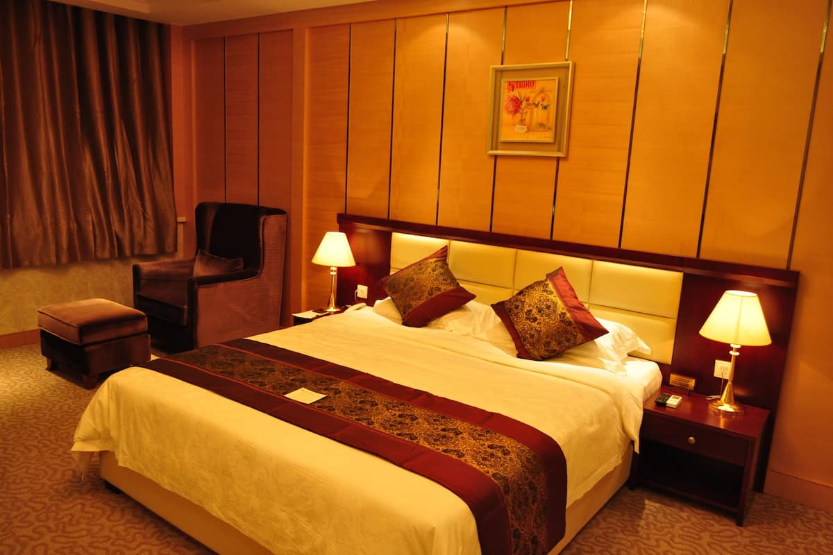 Ein Hotelzimmer mit einem großen Bett, zwei Nachttischlampen, einem Nachttisch, einem Sessel und einer Wandpaneele aus Holz.