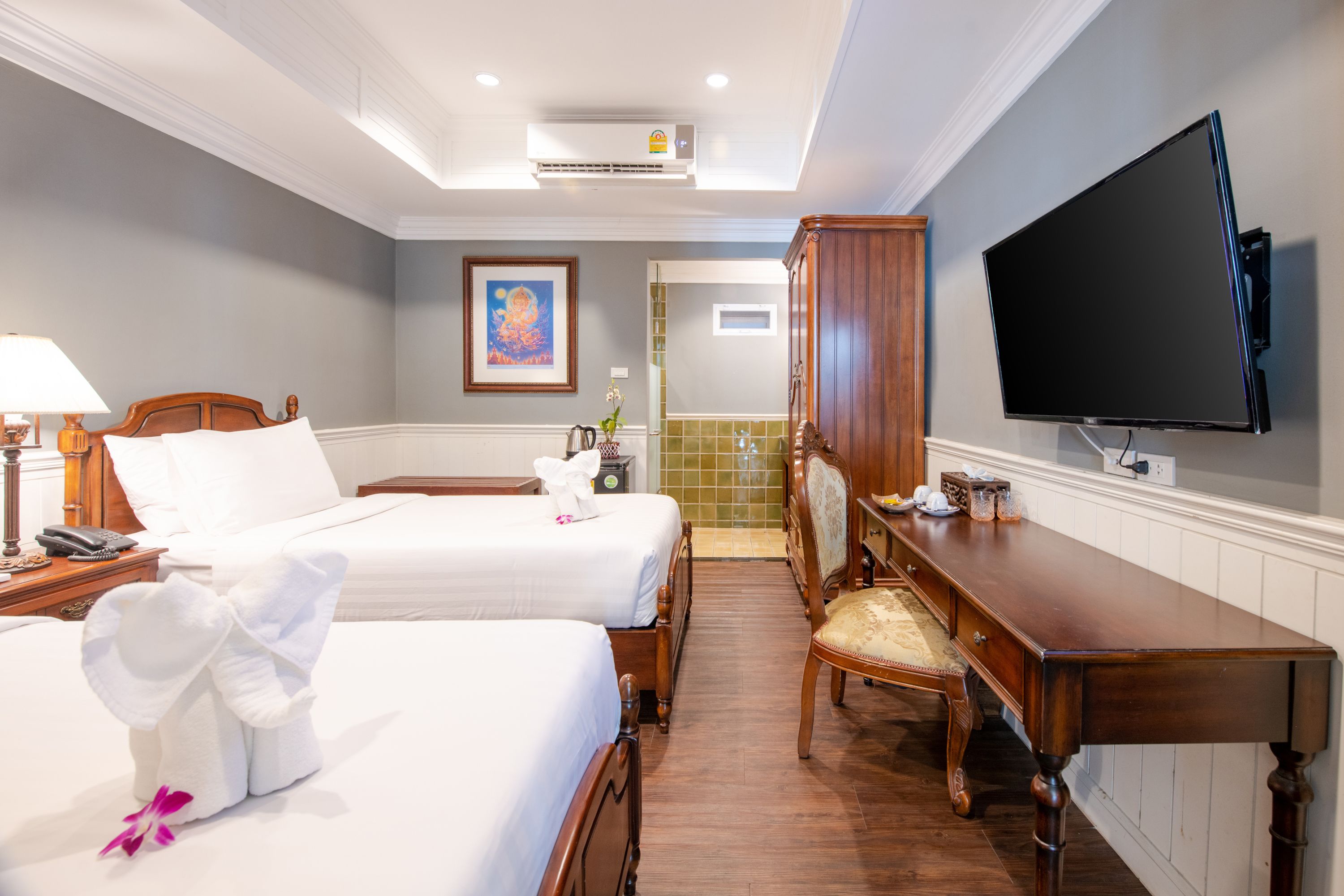 A hotel room with two beds, a desk, a television, and a bathroom visible through an open door.
