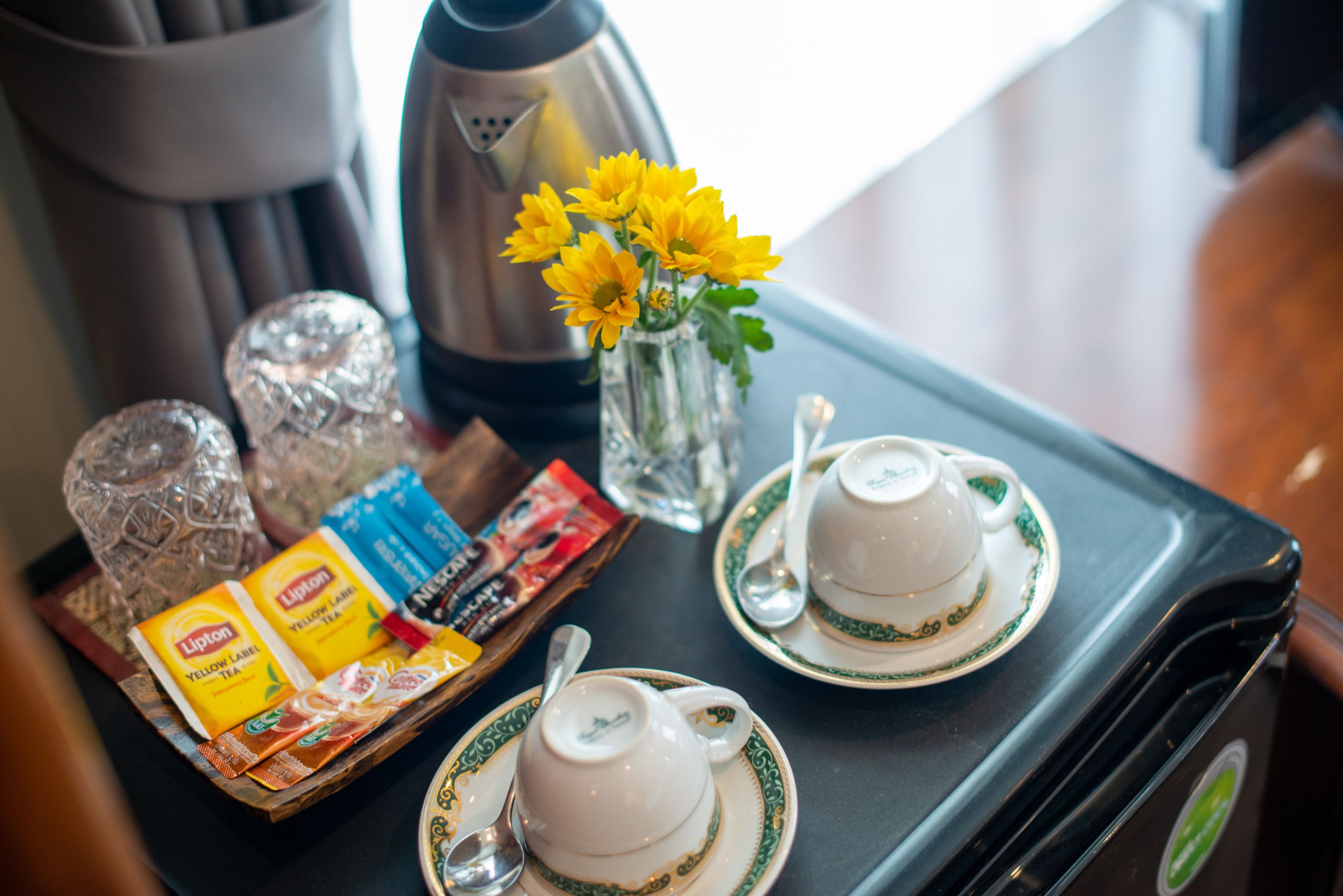 A tray with Lipton tea, a teapot, a cup, and a vase with yellow flowers on a table.