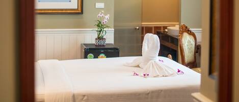 A hotel room with a bed, a framed picture on the wall, a small table with a vase, and a mirror reflecting the room.