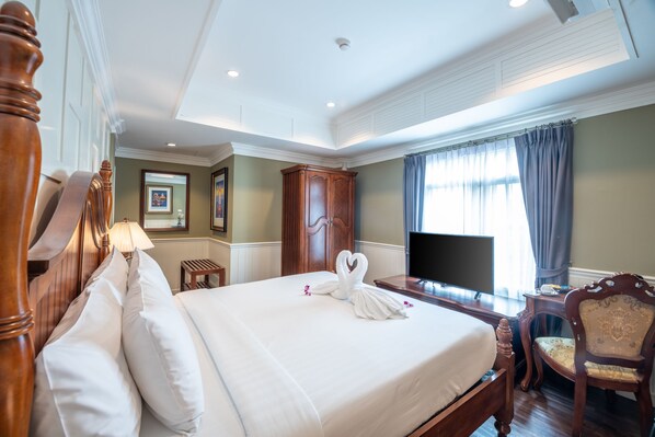 A hotel room with a large bed, wooden headboard, a television, a desk, and a chair. - The Orchid House 153 (Bangkok)