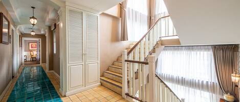 A hotel hallway with a tiled floor, a staircase, and a view of the dining area.
