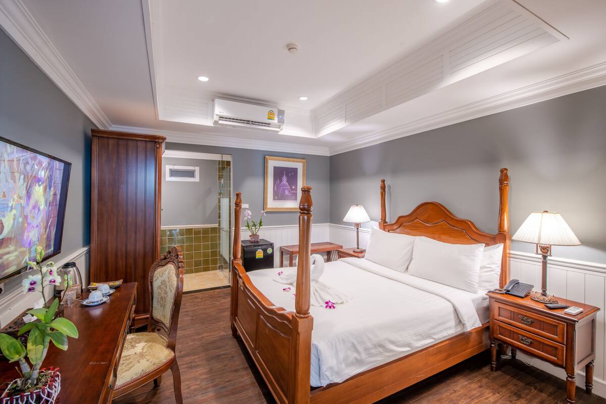 Une chambre d’hôtel avec un lit en bois, un bureau avec une chaise, une télévision et une salle de bain visible à travers une porte ouverte.