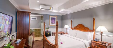 A hotel room with a wooden bed, bedside tables with lamps, a TV, and a dining area with a table and chairs.
