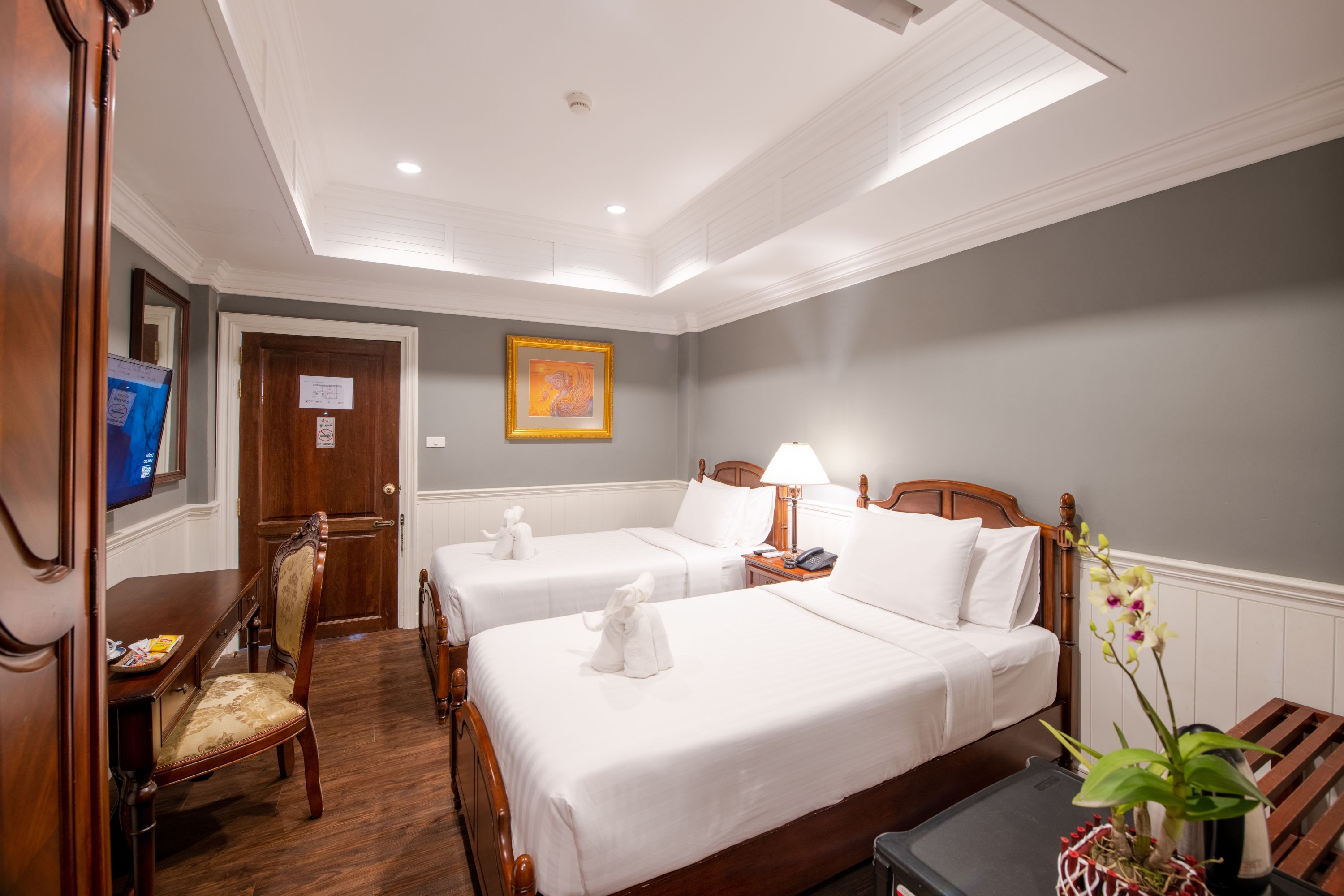Habitación de hotel con dos camas, un escritorio, una silla, una lámpara y una mesita con una planta.