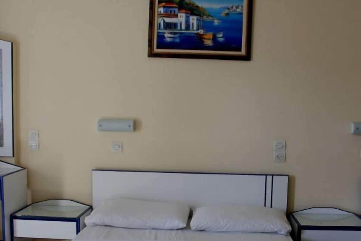 A hotel room with a bed, two bedside tables, a painting on the wall, and a red flower on the bed.