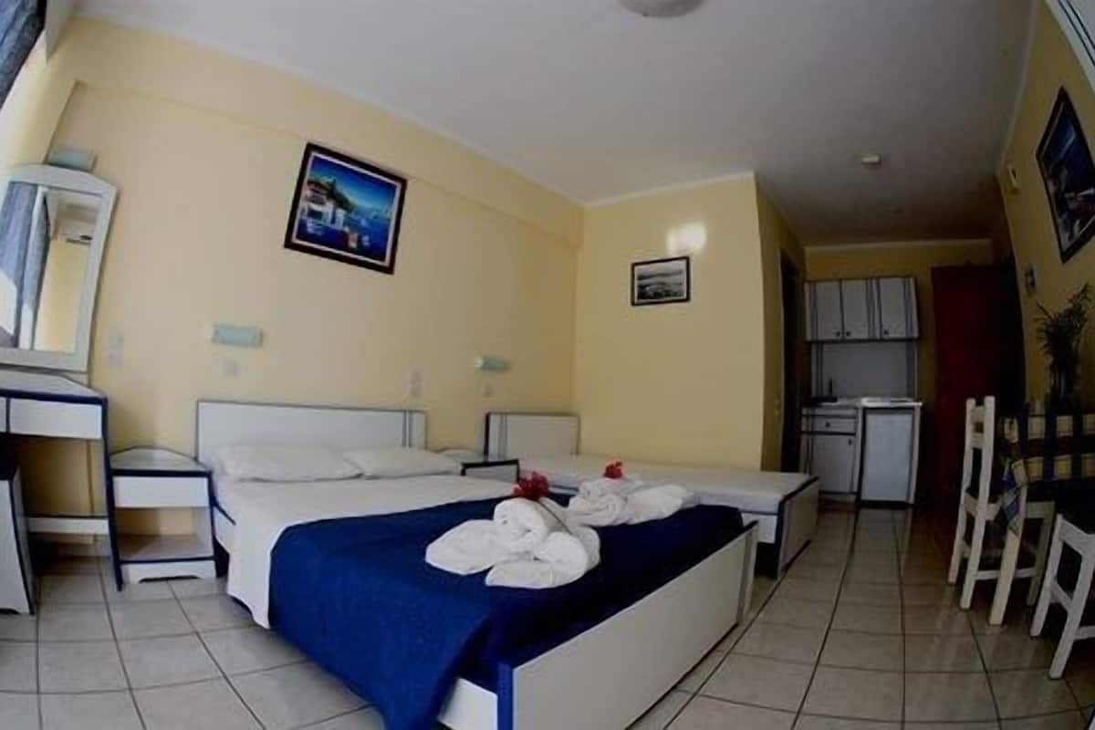 A hotel room with two beds, a desk, a chair, and a kitchenette.