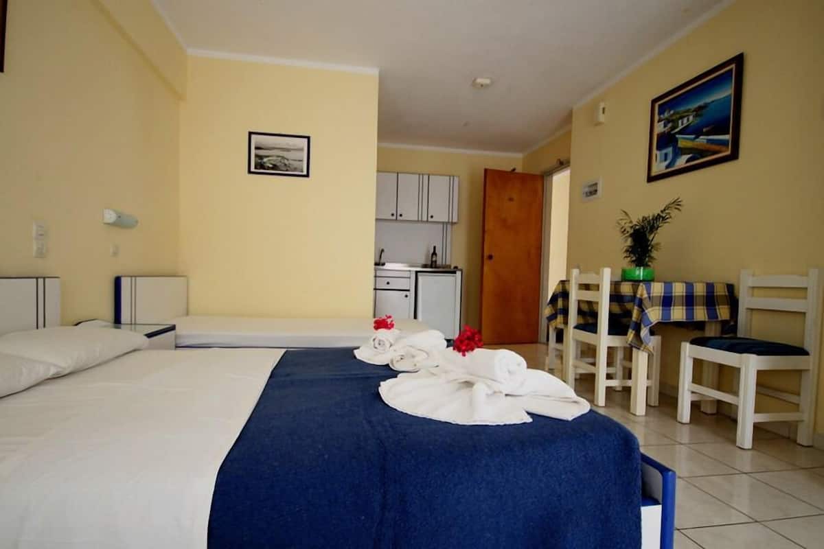 A hotel room with a bed, a desk, a chair, a small kitchenette, and a bathroom.