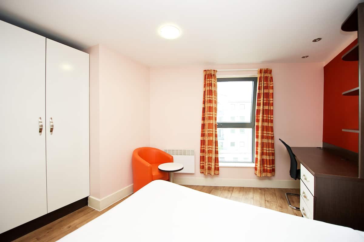 A small, modern room with a bed, a desk, and a chair.