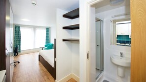 A hotel room with a bed, a desk, a chair, a window with curtains, a bathroom with a sink and mirror, and built-in shelves. - Citylivein Grove Street Edinburgh (Edinburgh)