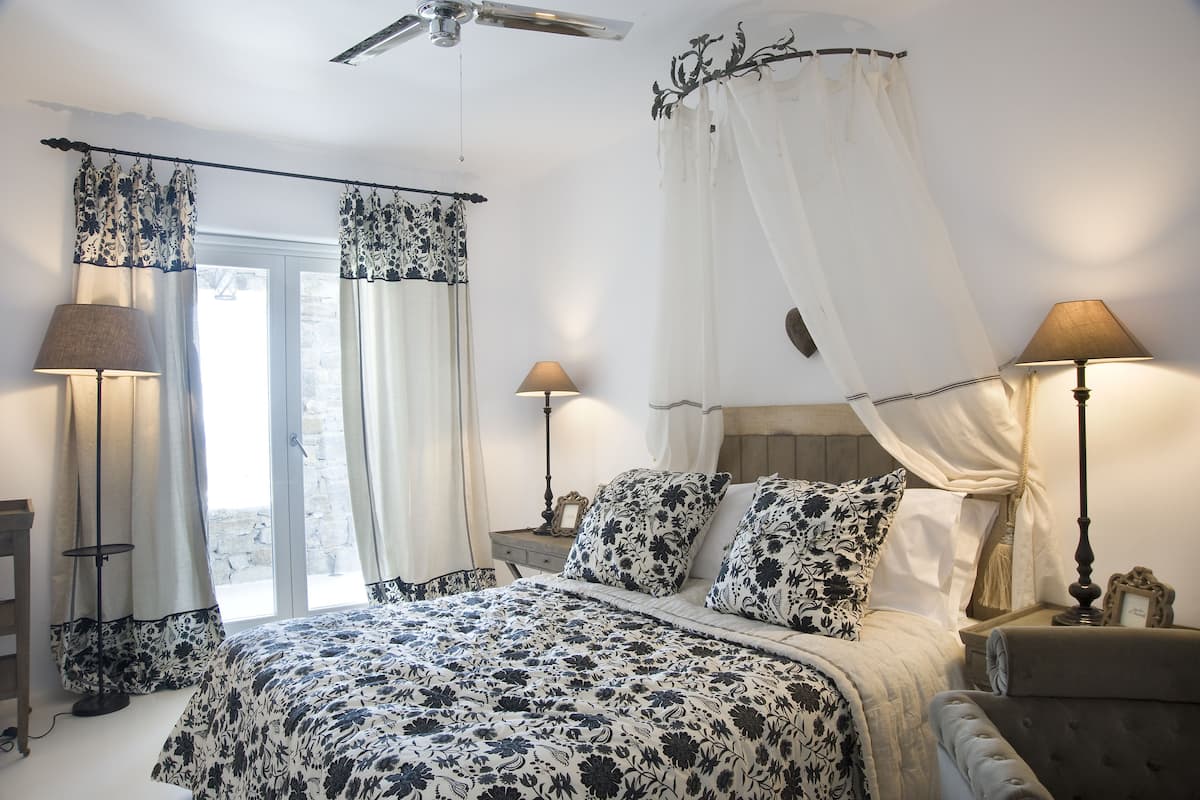 A bedroom with a bed, bedside lamps, a nightstand, a ceiling fan, and a window with curtains.