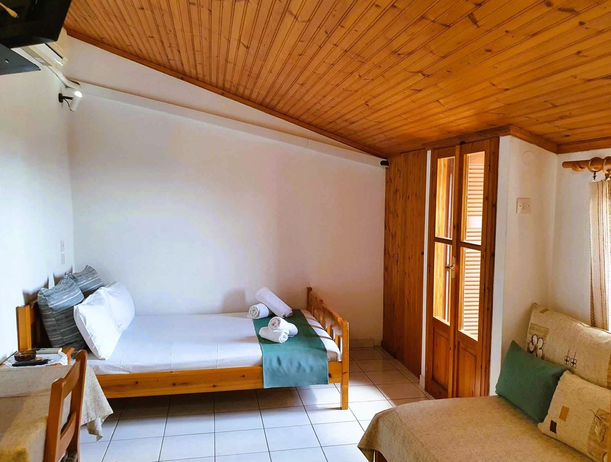 Quarto individual com piso e teto de madeira, e janela com persianas.