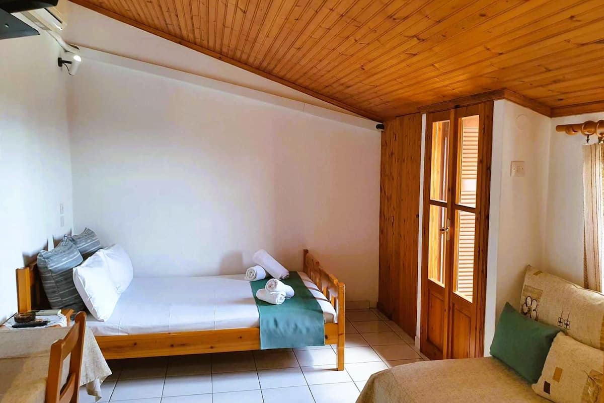 A small, cozy room with a wooden ceiling, a single bed with a green blanket, a wooden chair, and a small table.