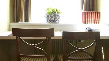 Two wooden chairs with striped cushions at a window sill, a potted plant, and a row of books on the windowsill.