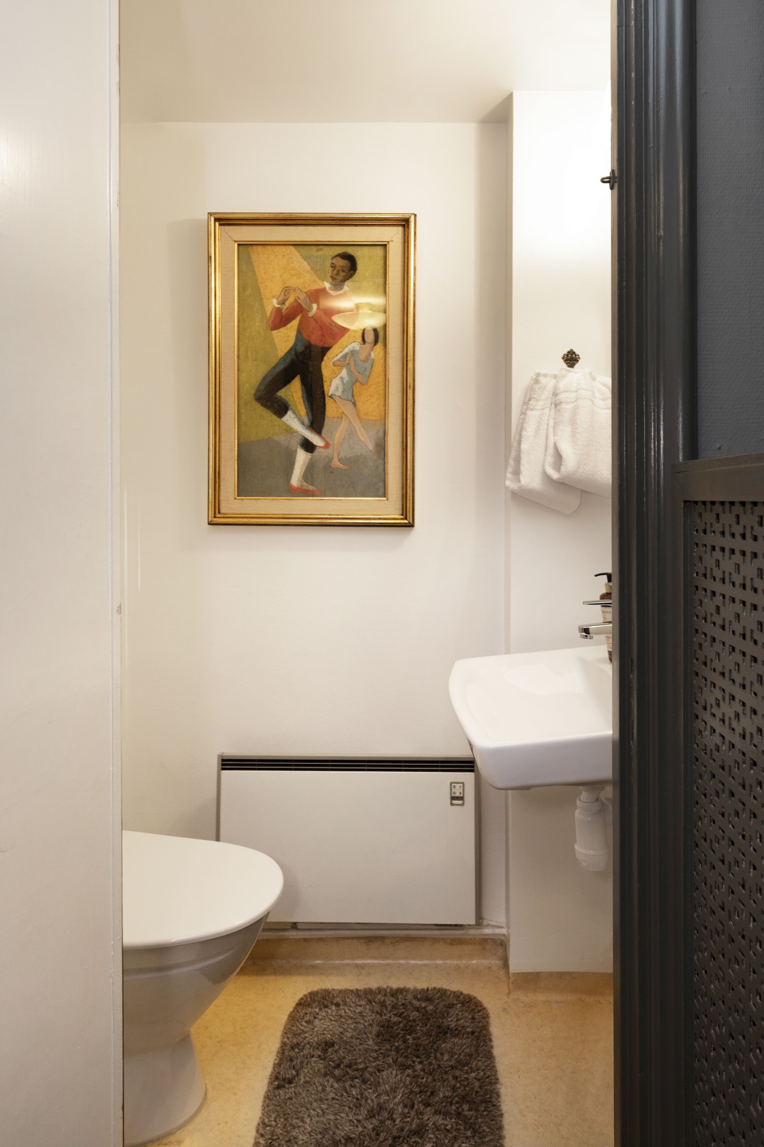 A bathroom with a toilet, sink, and a framed painting on the wall.
