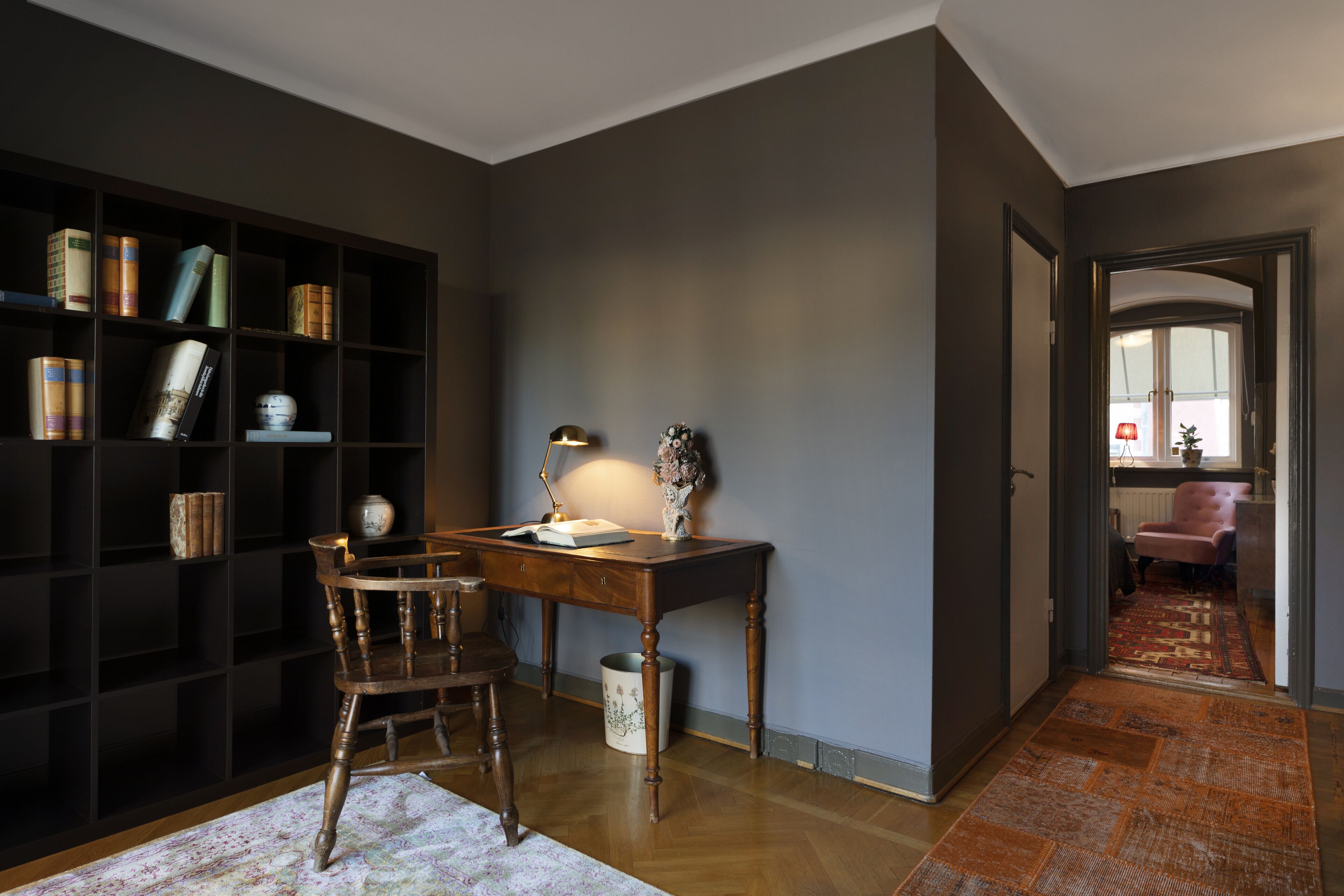 A study room with a wooden desk, a chair, a bookshelf, and a rug.