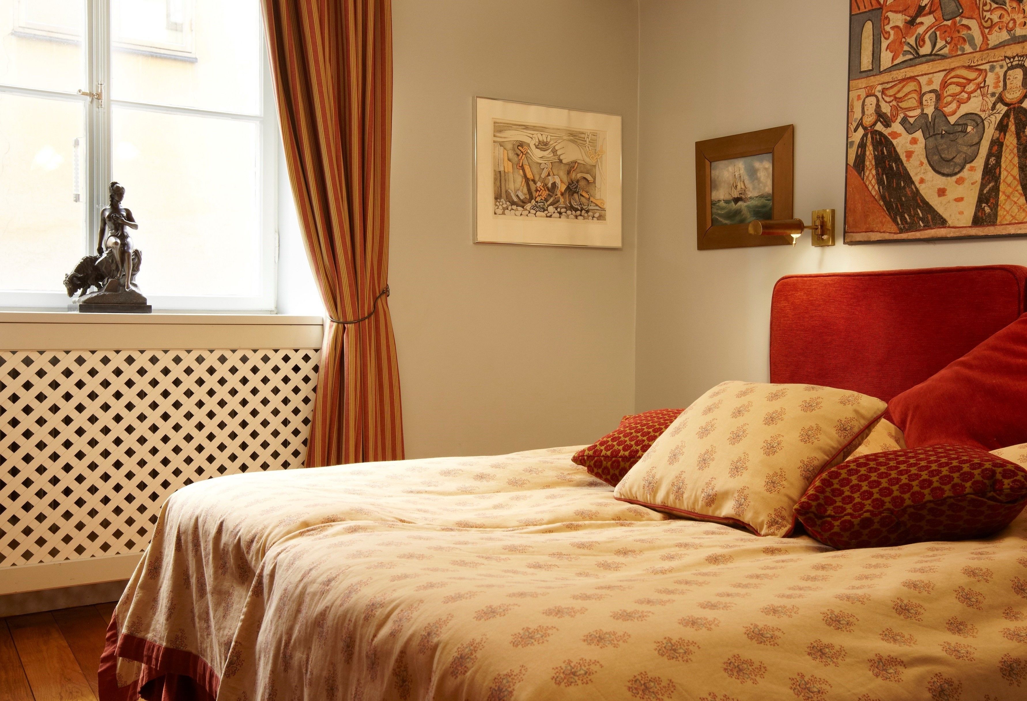A bedroom with a bed, a window with curtains, and artwork on the walls.