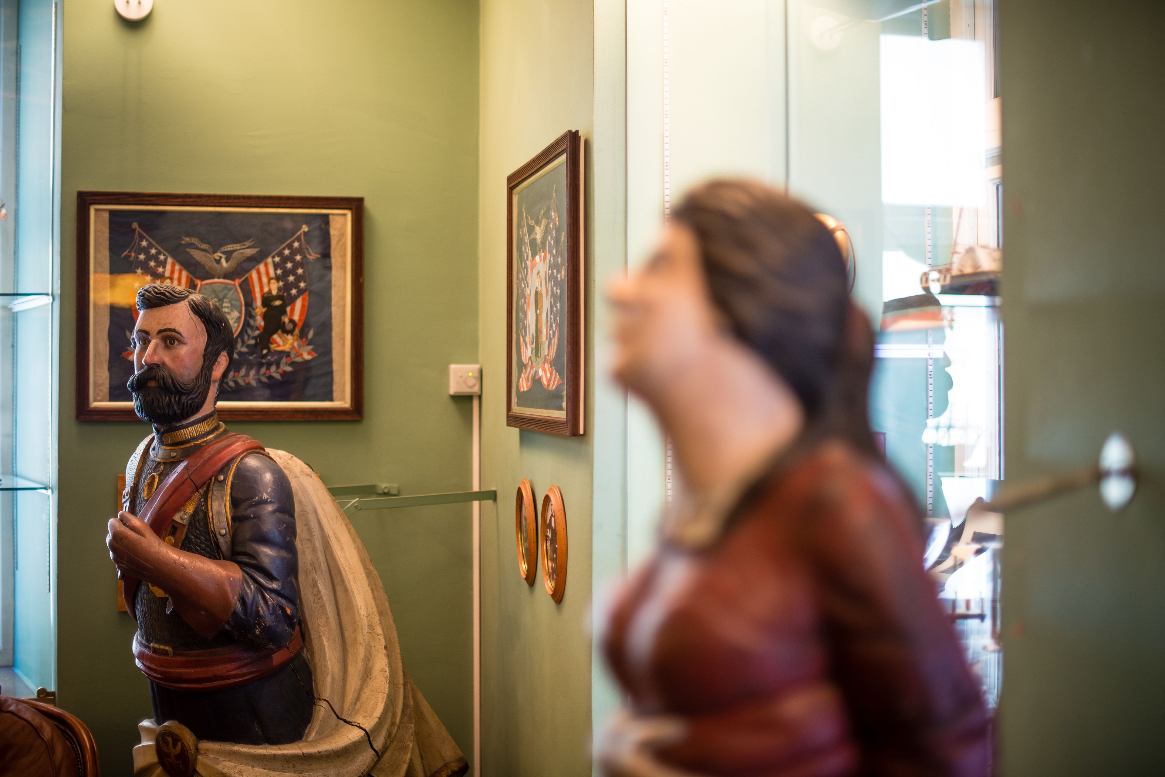 A statue in a room with framed artwork on the wall.