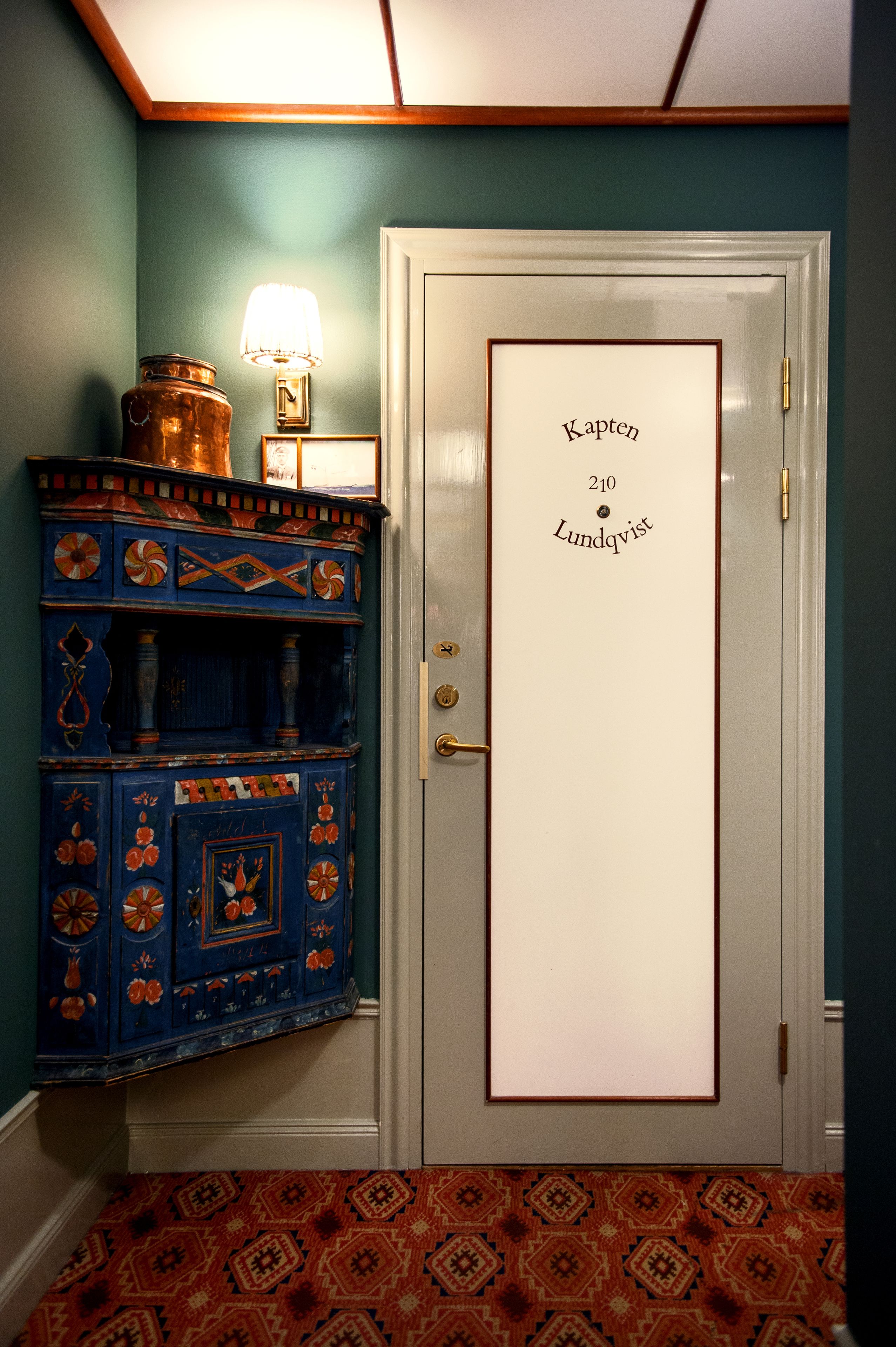 A door with a nameplate reading "Kapten 210 Lundqvist" and a blue cabinet with decorative patterns.