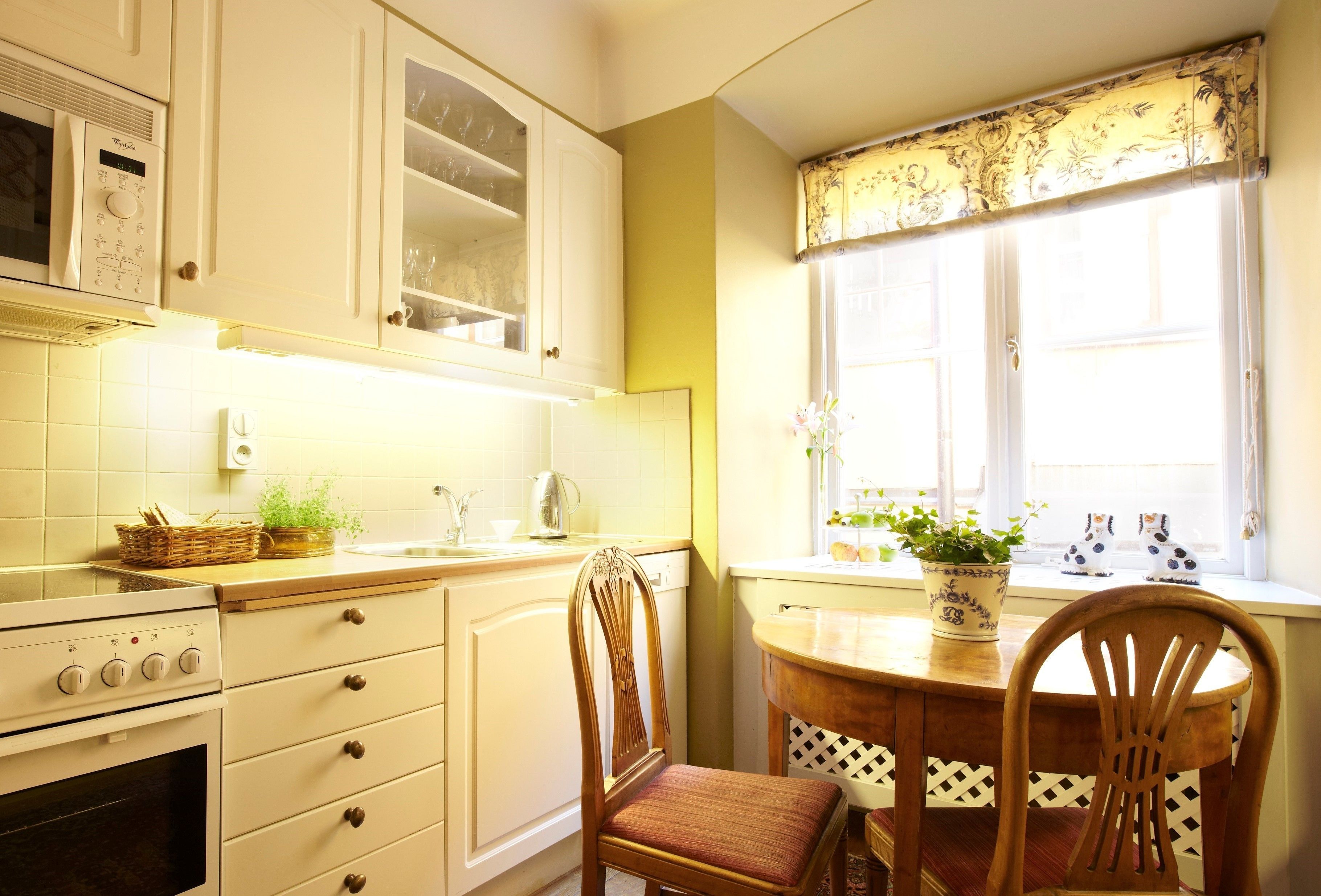 Una cocina con armarios blancos, estufa y ventana con cortina floral.