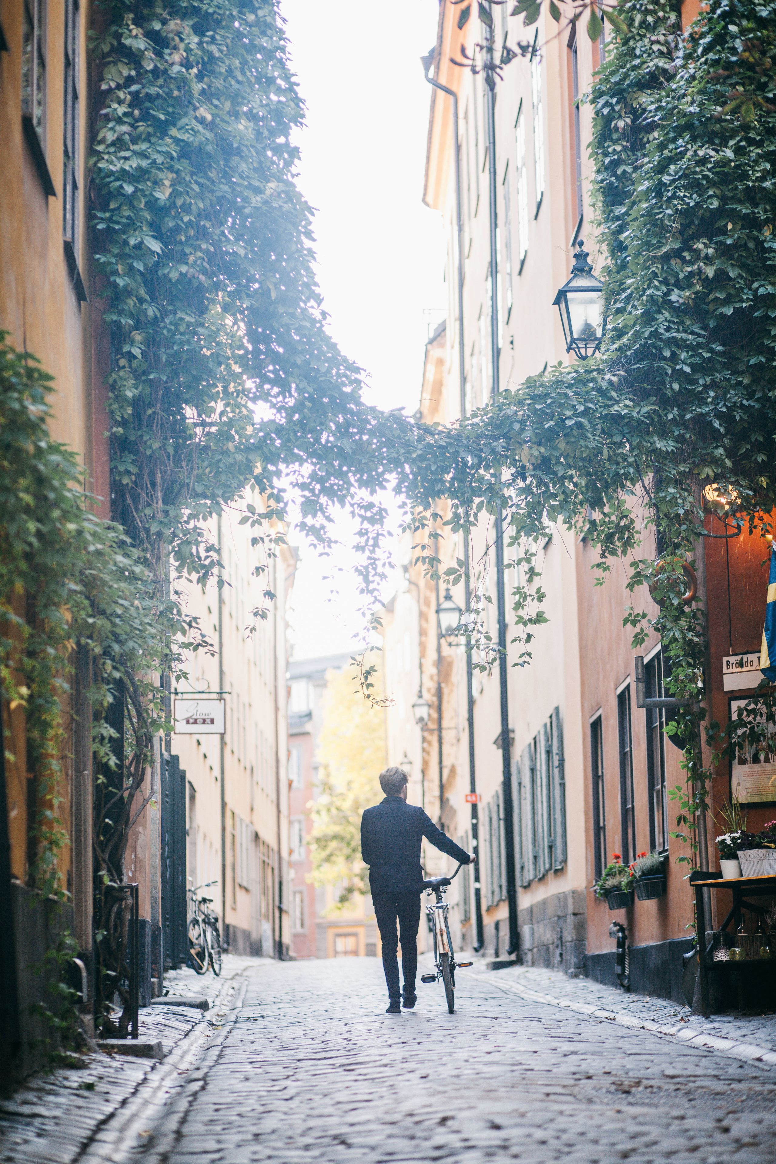 En brostensbelagt gade med bygninger, en person med en cykel, og et skilt med teksten "Bordo T".