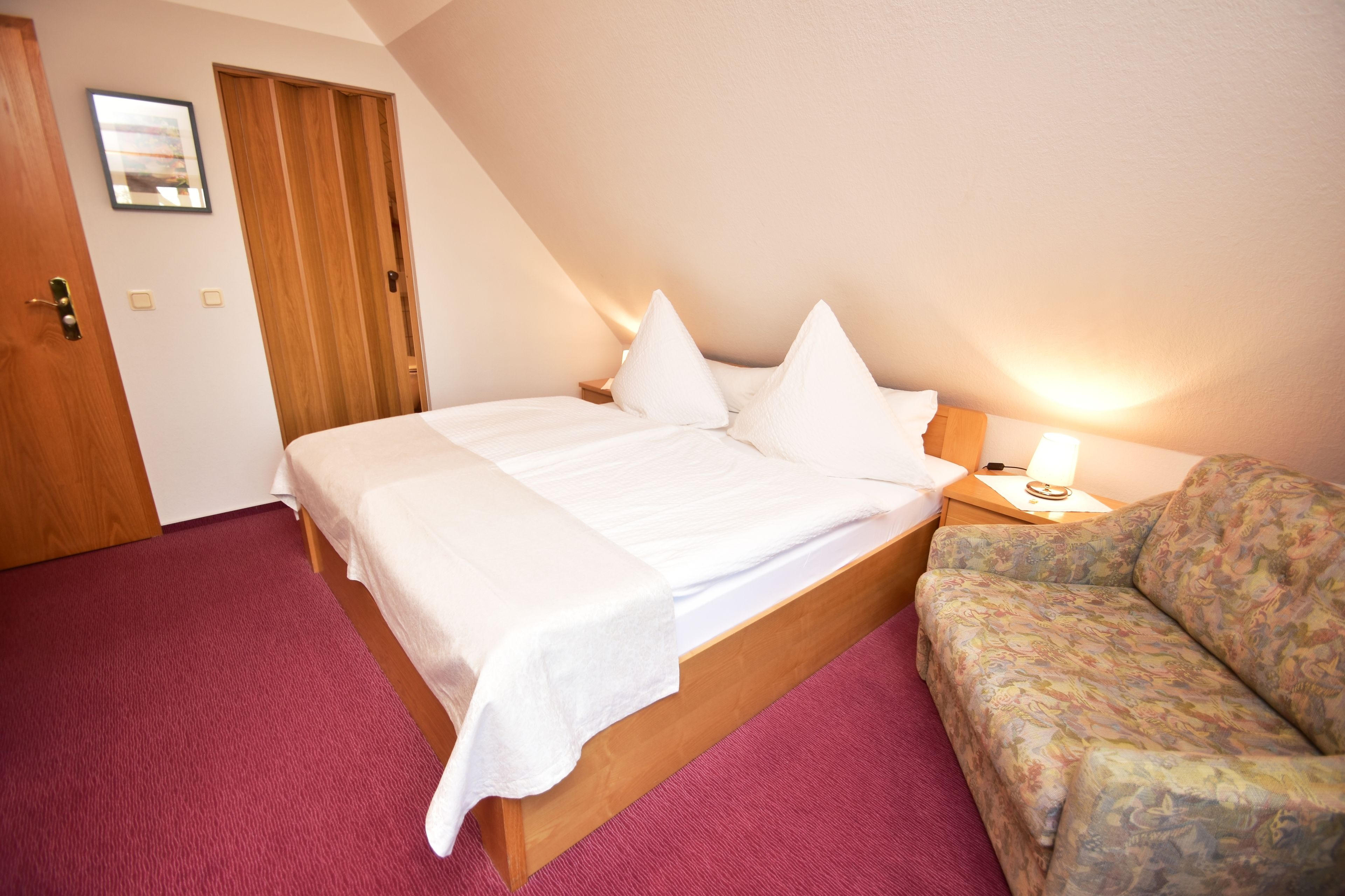 Ein Schlafzimmer mit einem hölzernen Bett, einem roten Teppich, einer Holztür und einem gerahmten Bild an der Wand.