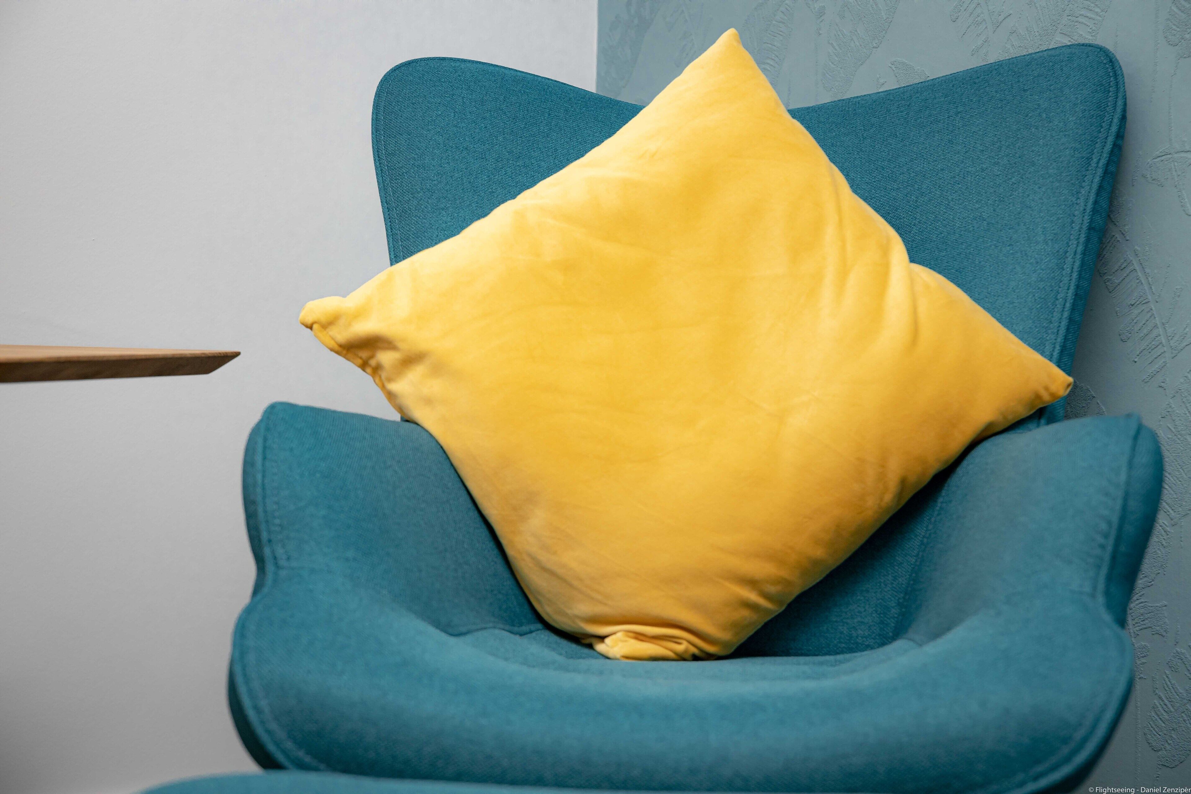 Un sillón azul turquesa con un cojín amarillo.